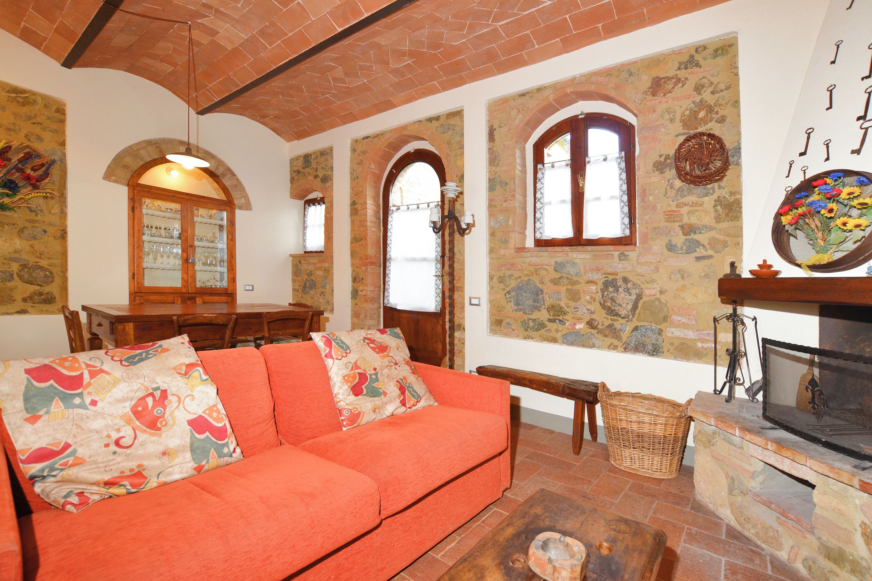 A cozy living room with a red sofa, stone walls, a fireplace, and a dining area with wooden furniture.