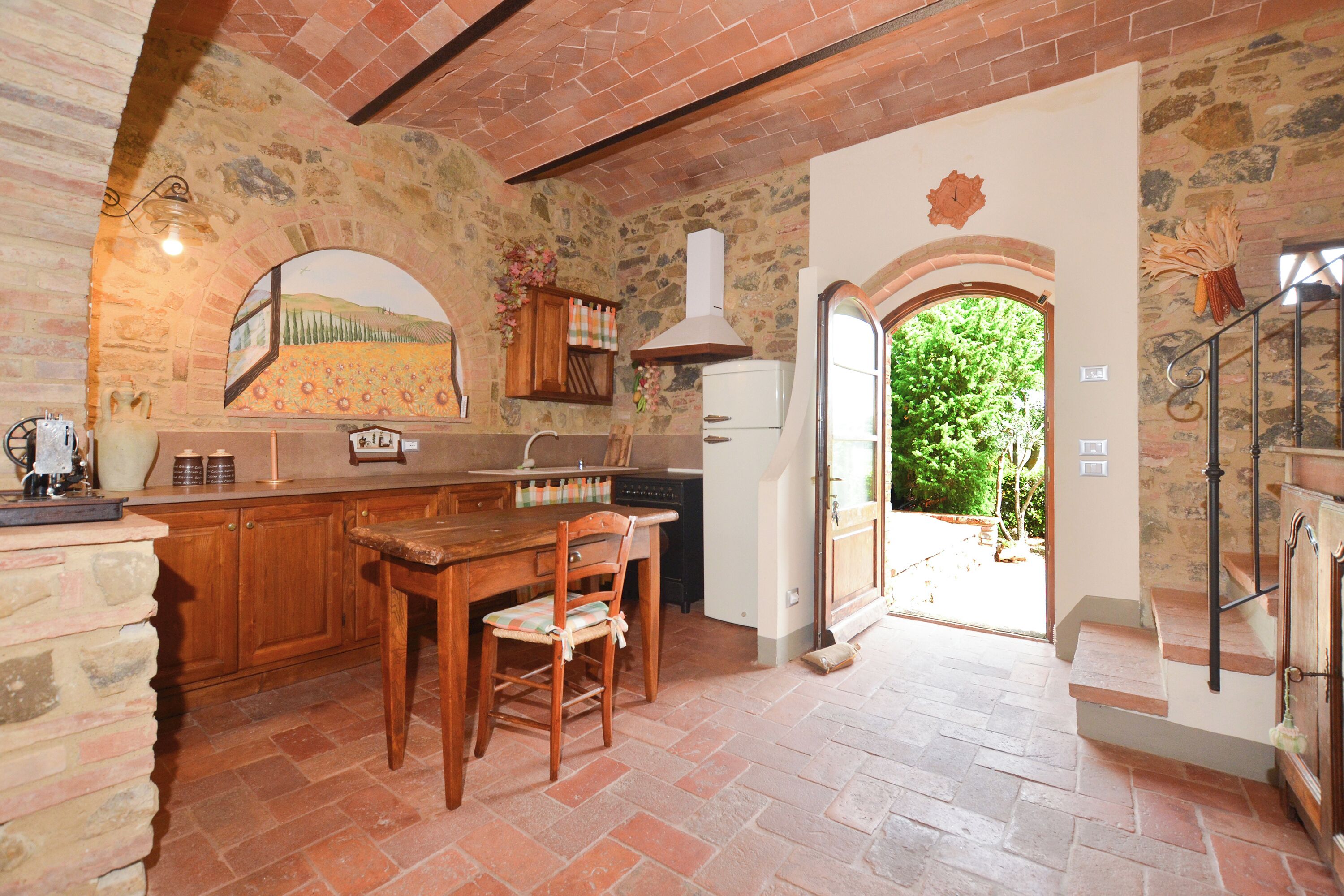 Una cocina rústica con paredes de piedra, una mesa de comedor de madera y vistas a un jardín a través de un vano abierto.