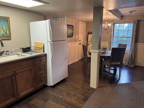 A kitchen with a refrigerator, wooden cabinets, a dining table with chairs, and a window with curtains. - Broad Street Studio-LOCATION! walk to town (Nevada City)