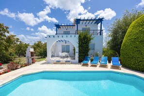 Un espace piscine avec une piscine à l’eau d’un bleu limpide, un bâtiment blanc doté d’un balcon et des chaises longues bleues.