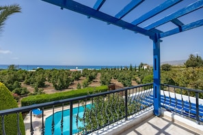 Un balcon avec vue sur une piscine, une végétation luxuriante et la mer.
