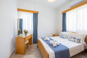 Quarto de hotel com uma cama de madeira, uma escrivaninha e um espelho.