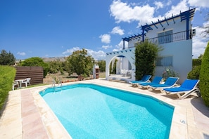 A swimming pool with lounge chairs, a pergola, and a view of the mountains.