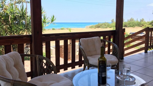 A covered outdoor seating area with wicker chairs and a table, overlooking a beach and ocean. - Villa Majestic in Agia Marina Chrysochous (Ayia Marina Chrysochous)