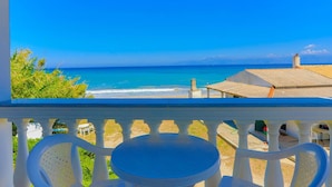 A balcony with a view of the ocean, a small table, and white chairs.