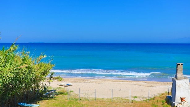 A beach with clear blue water, a sandy shore, and a few beach chairs.