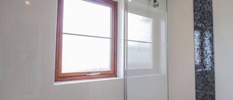 Ein Badezimmer mit Duschkabine aus Glas, einem Fenster mit Holzrahmen und einer Wand mit Musterfliesen.