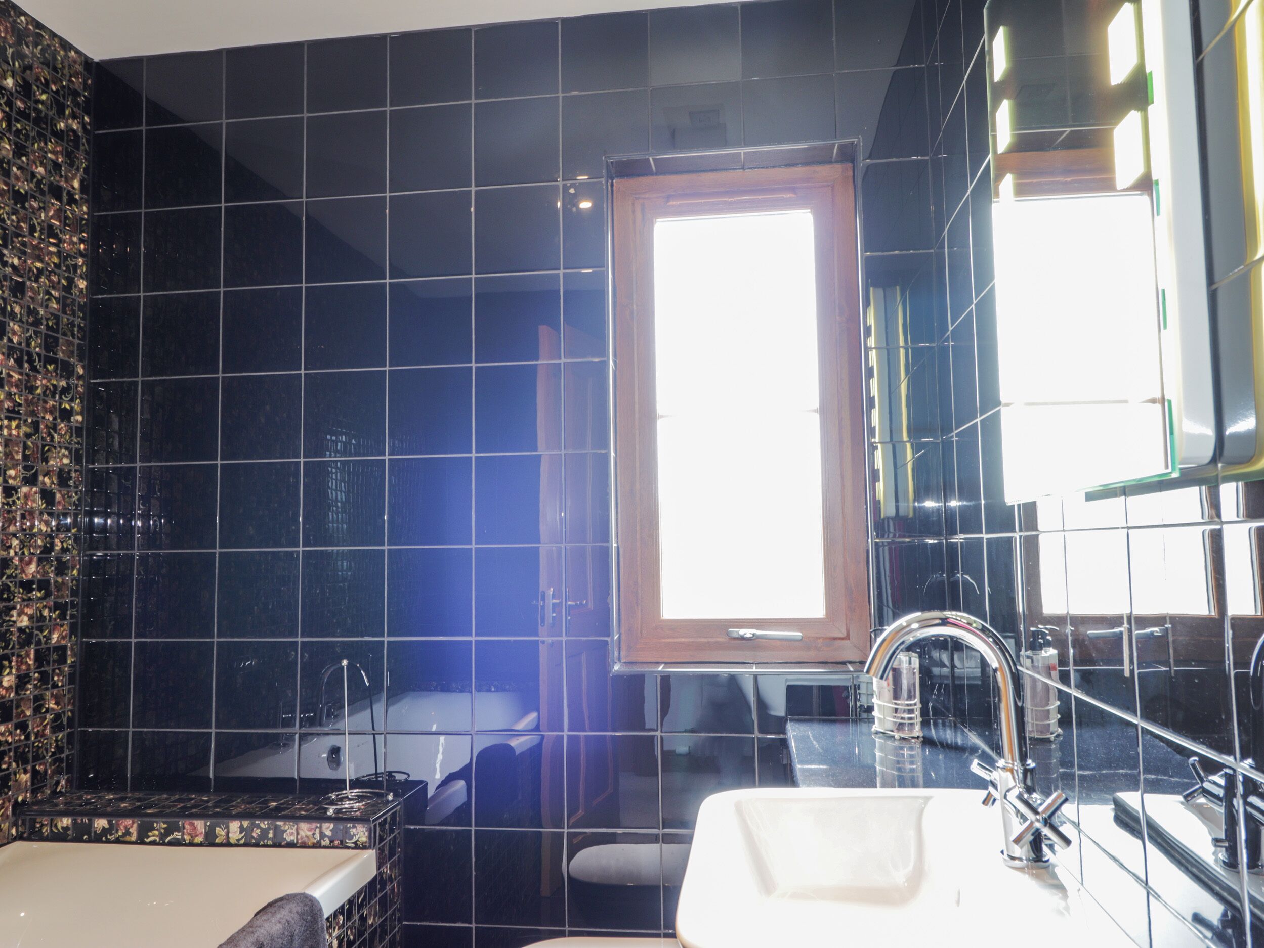 Ein modernes Badezimmer mit schwarzen Fliesen, einer Badewanne, einem Waschbecken und einem Fenster.