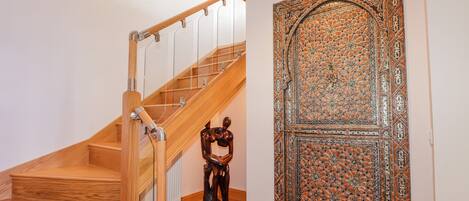 A wooden staircase with glass railings, a decorative door with intricate patterns, and a small sculpture on the floor.