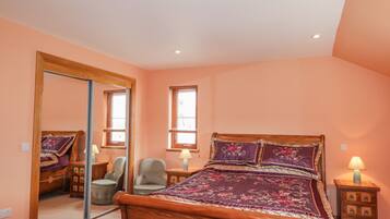 A bedroom with a wooden bed, a large mirror, two bedside tables with lamps, and a window with blinds.