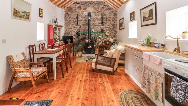 Un intérieur chaleureux avec une cheminée en pierre, des poutres apparentes en bois au plafond et un coin repas comprenant des chaises et une table.