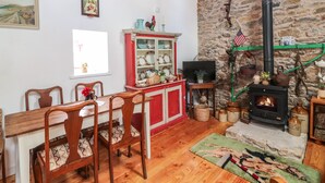 Un salon chaleureux avec un mur en pierre, une cheminée, une table à manger en bois avec des chaises, un buffet rouge et un téléviseur.