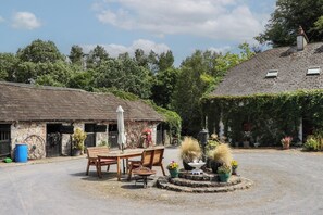 A rustic outdoor seating area with a table and chairs, surrounded by potted plants and a decorative fountain. - The Dairy (Ardfinnan)