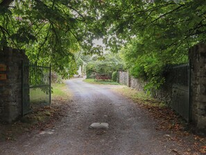 A paved pathway leading through a gated area with stone walls and lush greenery overhead.