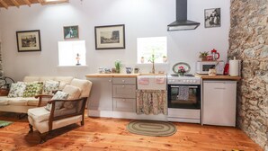 Une cuisine chaleureuse avec un plancher en bois, un poêle blanc et un mur en pierre.