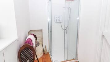 A bathroom with a glass shower enclosure, a wooden chair with towels, and a white sink.