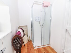 Un baño con cabina de ducha de vidrio, una silla de madera con toallas y un lavamanos blanco.