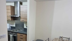 A compact kitchen with wooden cabinets, a stainless steel range hood, and a small dining area with a table and chairs. - Central 2-bedroom Apartment, Chelmsford, Parking (Chelmsford)