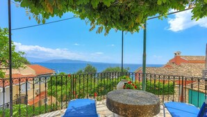 Un balcón con una mesa de piedra, sillas azules y vista al mar.