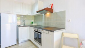 Una cocina compacta con armarios blancos, horno empotrado, pileta de acero inoxidable y una pequeña encimera.