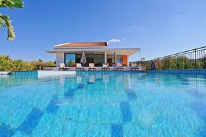 Un hôtel moderne doté d’une piscine, de chaises longues et d’un patio couvert.