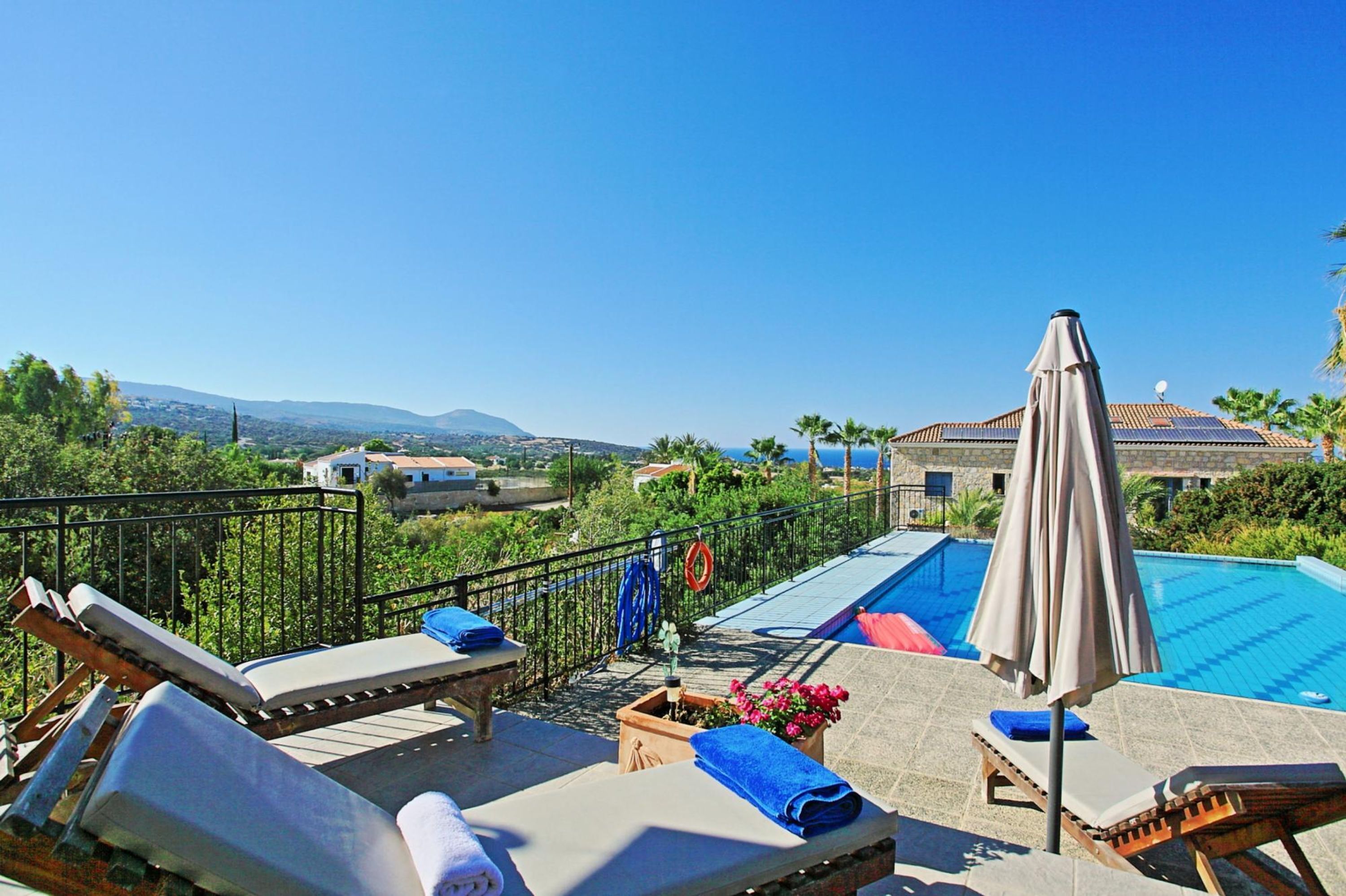 A rooftop pool area with lounge chairs and umbrellas, surrounded by a metal fence and a view of the landscape.