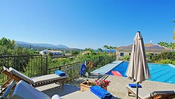 A rooftop pool area with lounge chairs and umbrellas, surrounded by a metal fence and a view of the landscape.