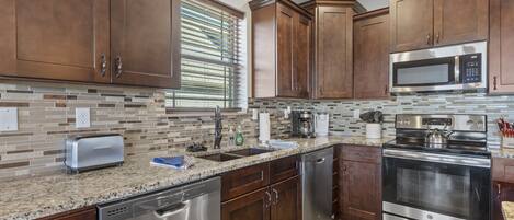 A modern kitchen with stainless steel appliances, wooden cabinets, and a tiled backsplash.
