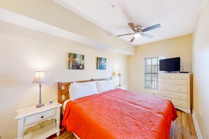 A bedroom with a bed, nightstands, a dresser, a ceiling fan, and a TV.