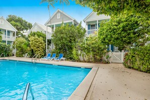 Relax by the serene pool surrounded by lush greenery and a white picket fence.