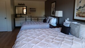 A hotel room with two beds, a desk, a chair, a mirror, and a painting on the wall. - Furnas County Lodging (Beaver City)