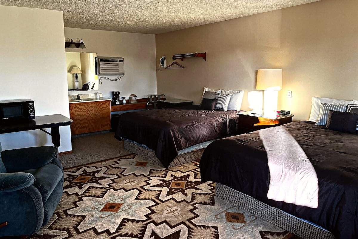A hotel room with two beds, a desk, a chair, a microwave, a coffee maker, and a hanging coat rack.