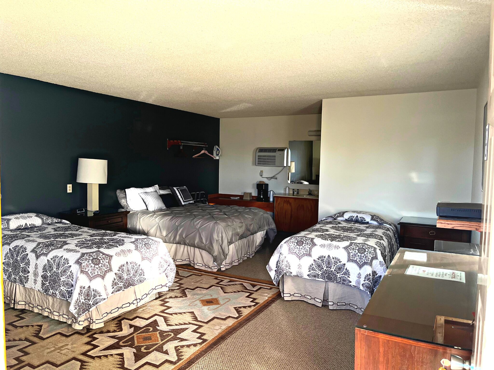 A hotel room with two beds, a desk, a dresser, a mirror, and a wall-mounted air conditioner.