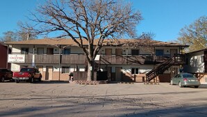 A motel with a two-story building, a parking lot, and a tree in front. - Furnas County Lodging (Beaver City)
