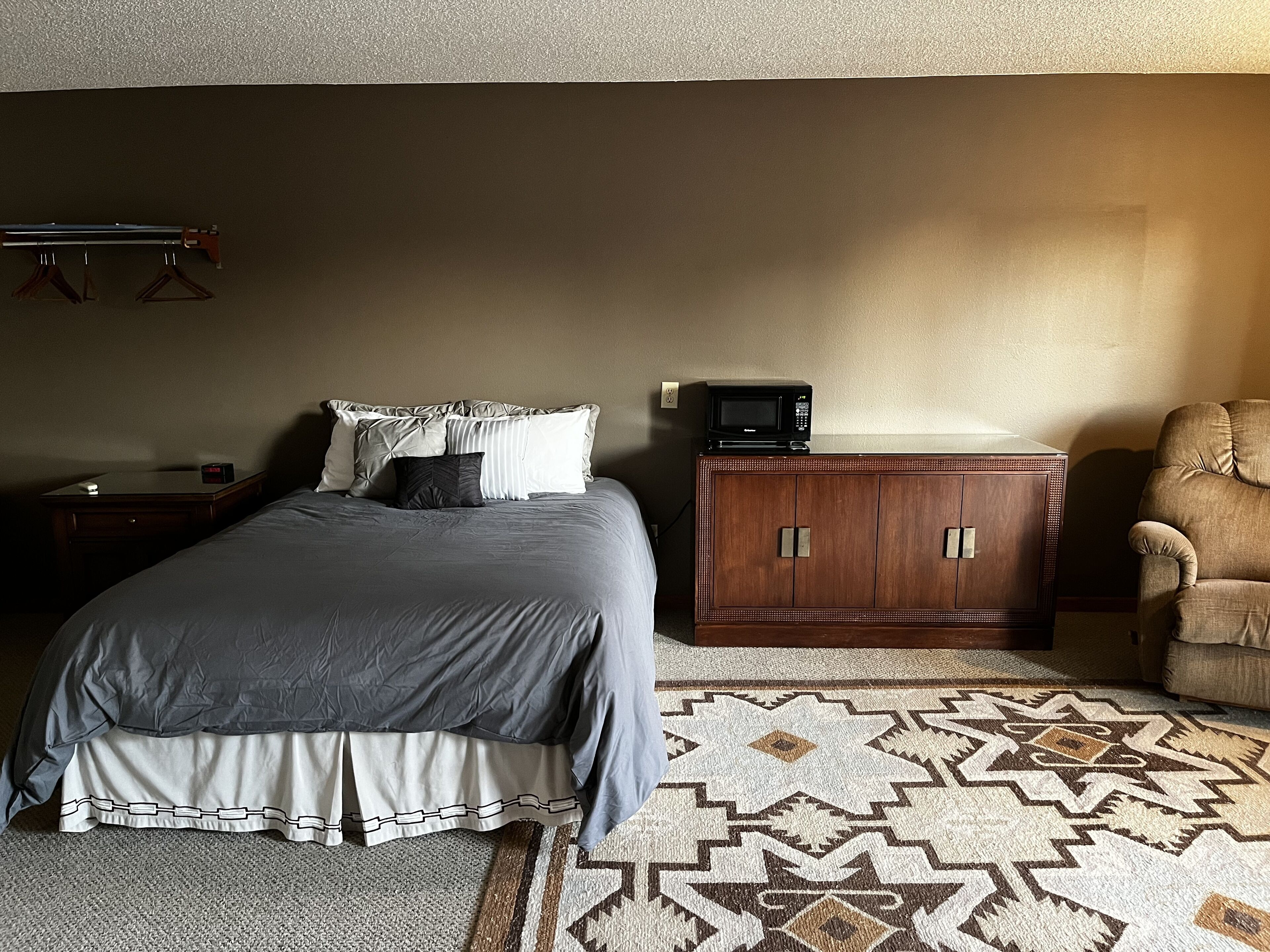 A bedroom with a bed, a wooden cabinet, a chair, and a patterned rug.