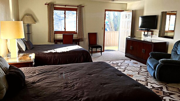 A hotel room with two beds, a desk, a chair, a TV, and a balcony. - Furnas County Lodging (Beaver City)