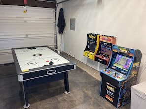 Une pièce avec un baby-foot, deux jeux d’arcade et une porte blanche.