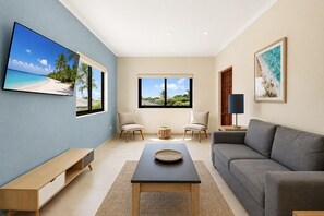 Un salon moderne comprenant un téléviseur, deux fauteuils, un canapé, une table basse et une fenêtre donnant sur un paysage verdoyant.