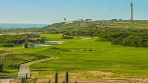Ein Golfplatz mit Bunkern, einem Wasserschutzhindernis, einem Leuchtturm und einem Gebäude auf einem Hügel.