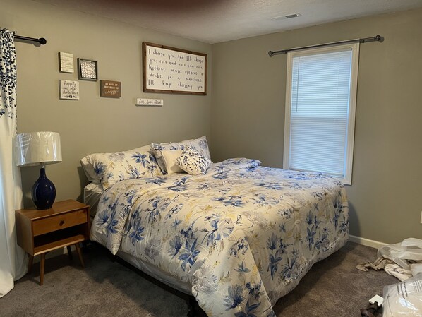 Cozy retreat with a neatly made bed, wooden nightstand, and inspirational quote on the wall.