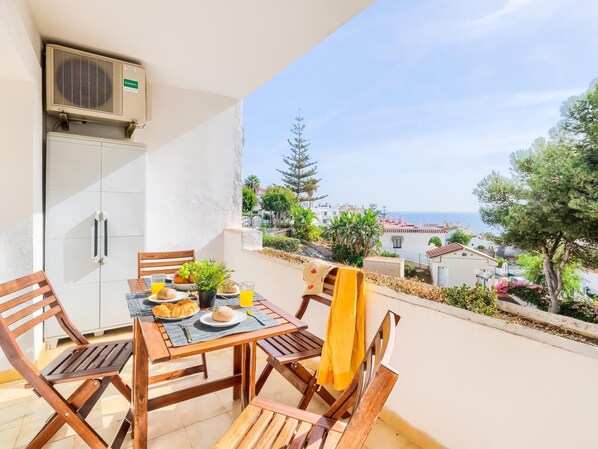 Un balcon avec une table préparée pour le petit-déjeuner, comprenant des croissants, une plante et du jus d’orange.