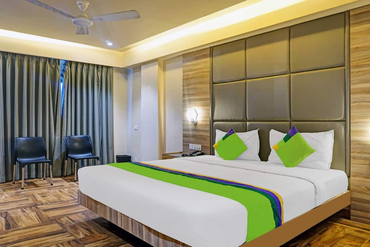 A hotel room with a large bed, two chairs, a ceiling fan, and a wooden floor.