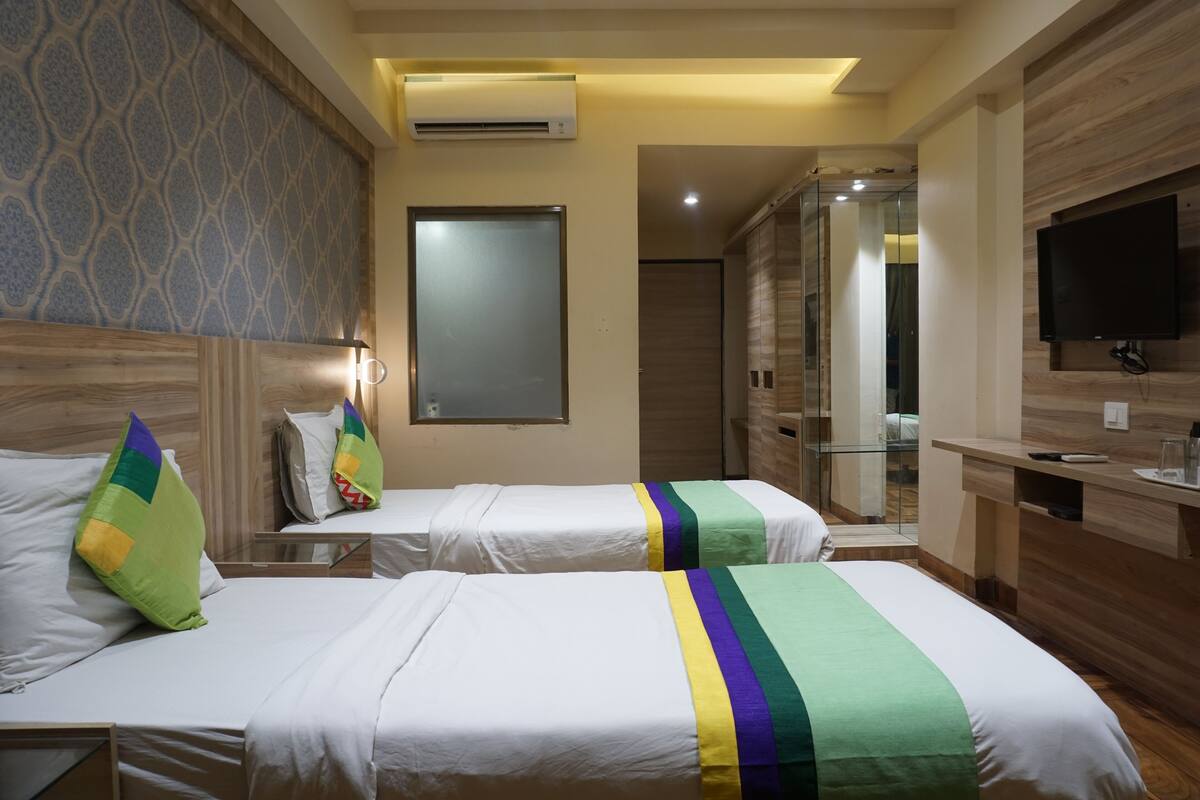 A hotel room with two beds, a TV, a mirror, and a shower area.