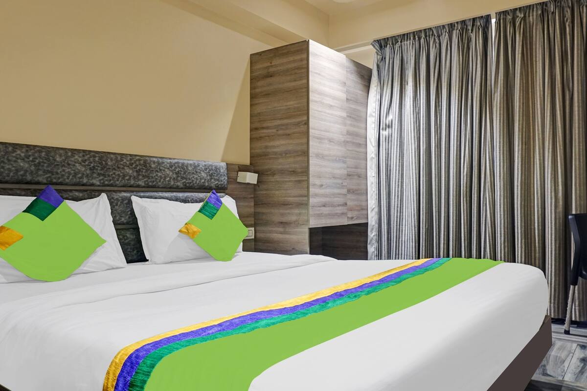 A hotel room with a large bed, two pillows, a nightstand, a chair, and a curtain.