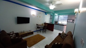 A living room with a sofa set, a coffee table, a TV mounted on the wall, and a kitchen area with cabinets and a sink. - Cozy vacation retreat (Roseau)