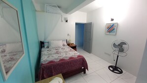A bedroom with a bed, bedside table, lamp, and a standing fan. - Cozy vacation retreat (Roseau)