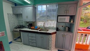 A compact kitchen with grey cabinets, a microwave, and a gas stove. - Cozy vacation retreat (Roseau)