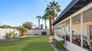 A covered patio area with outdoor seating, a well-maintained lawn, and palm trees.
