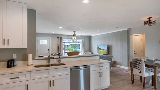 A modern kitchen with white cabinets, a dishwasher, and a large window.