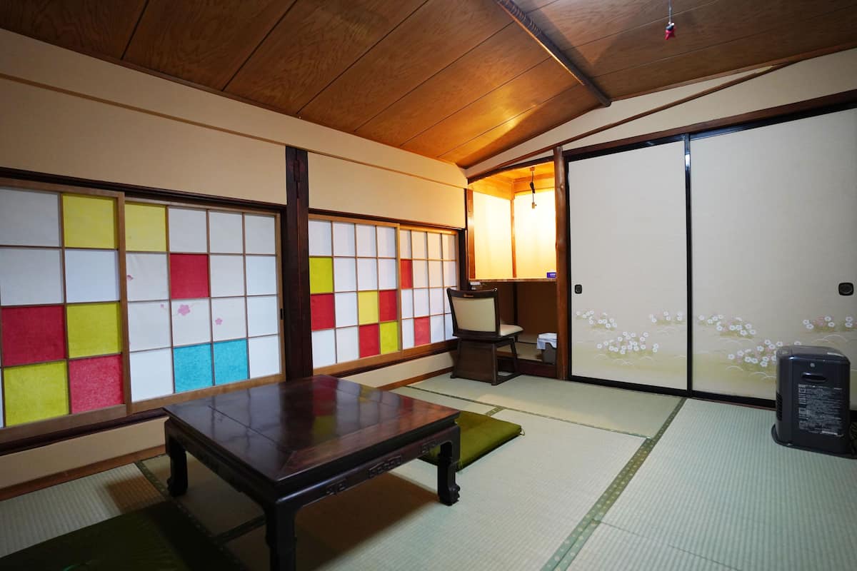 Ett traditionellt japanskt rum med tatamimattor på golvet, ett lågt träbord, en grön kudde och en skjutdörr med ett blommönster.